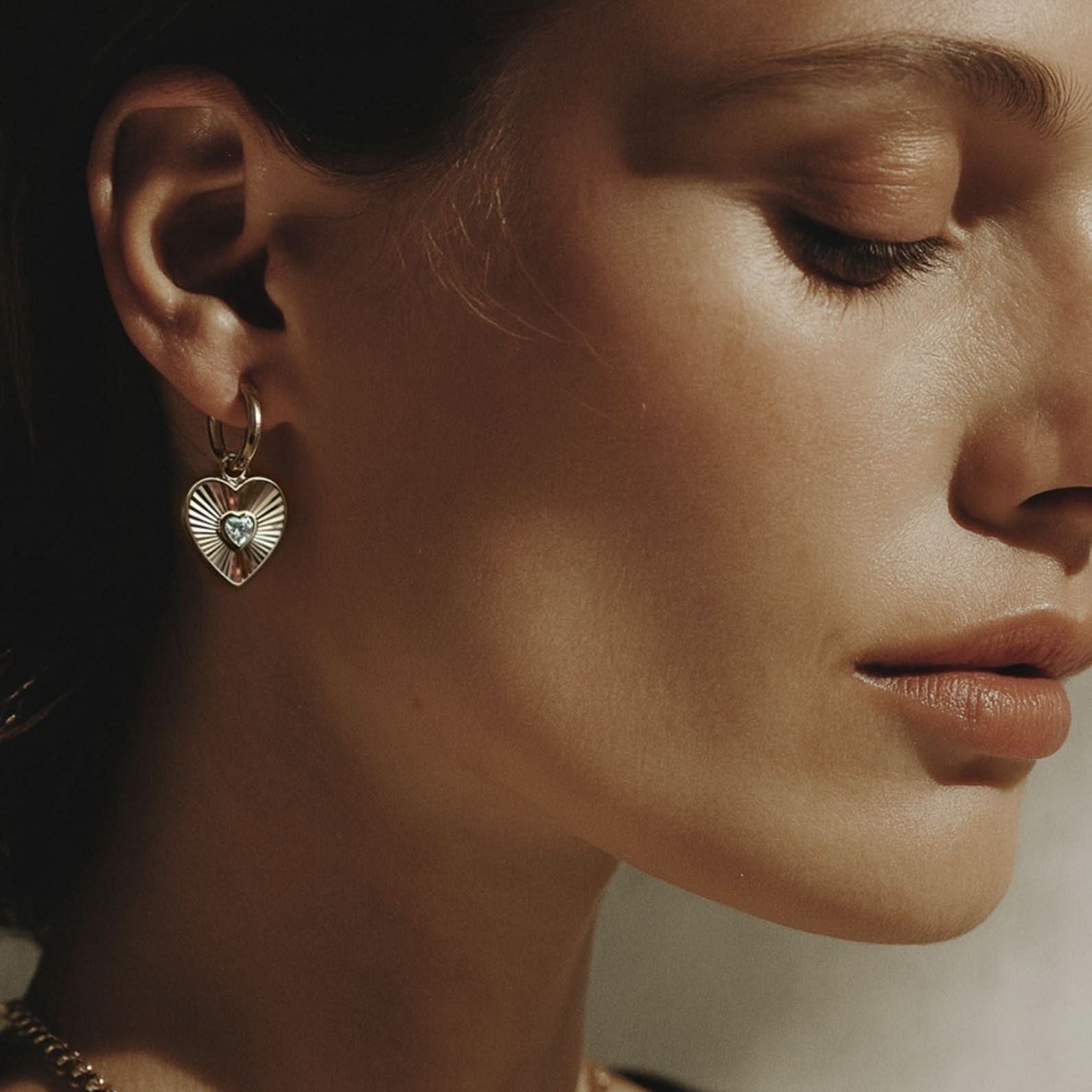 Close-up of a woman wearing heart-shaped earrings and layered necklaces.