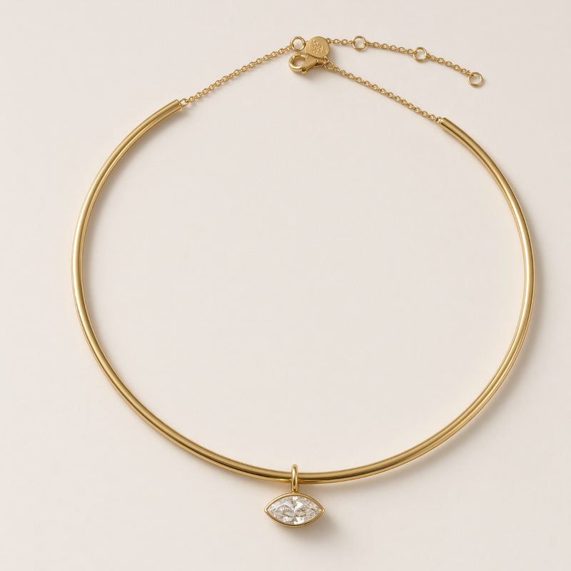 A gold-toned bangle necklace with a small marquise-cut clear gemstone pendant, displayed on a light beige background.