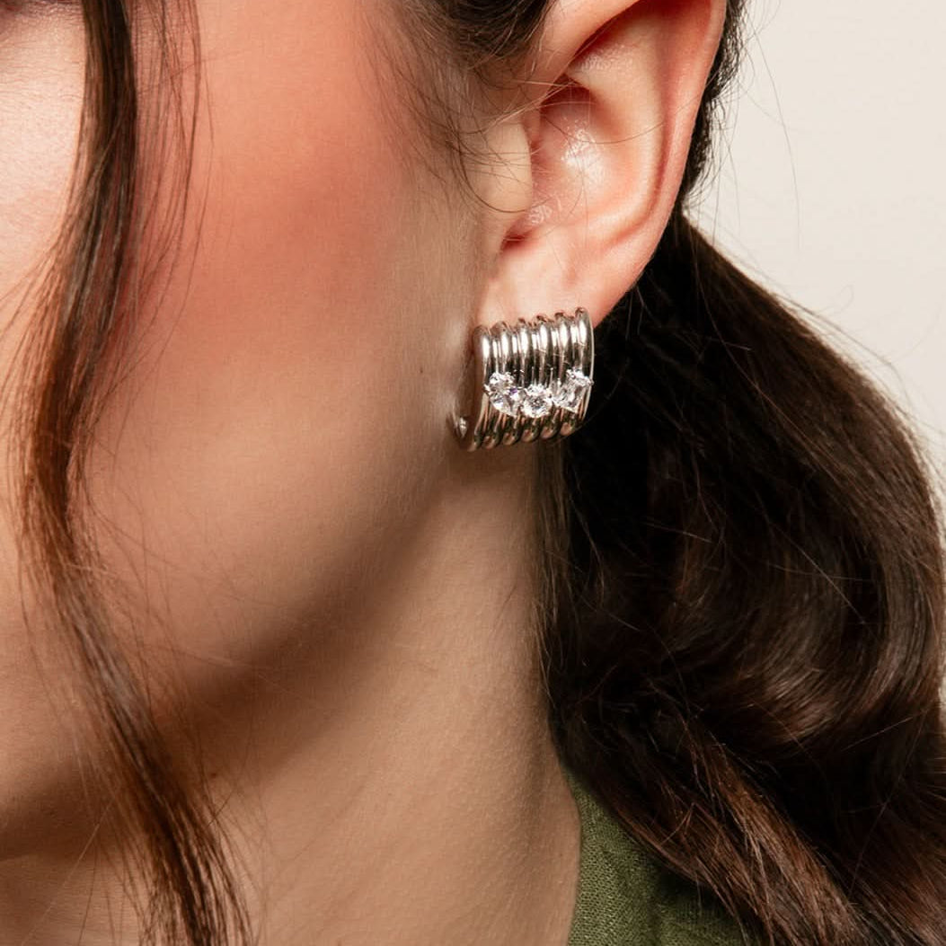 Close-up of a person wearing silver hoop earrings with a neutral background