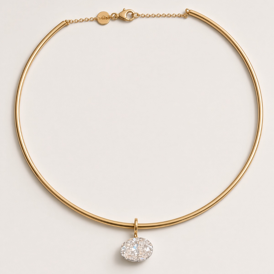 A gold-toned choker necklace with a delicate chain, a small circular charm, and a central cluster of clear pavé gemstones, displayed on a light beige background.
